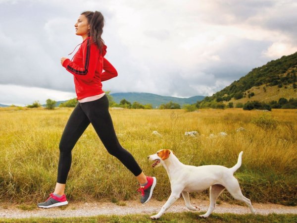 Mujer corriendo con un perro al aire libre, disfrutando de la actividad física.