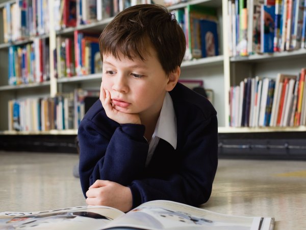 Un niño pequeño acostado en el suelo, leyendo un libro.