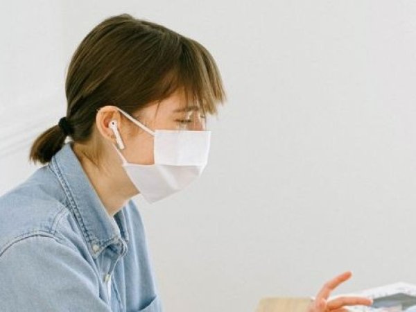 Mujer joven usando mascarilla mientras está sentada escuchando música.