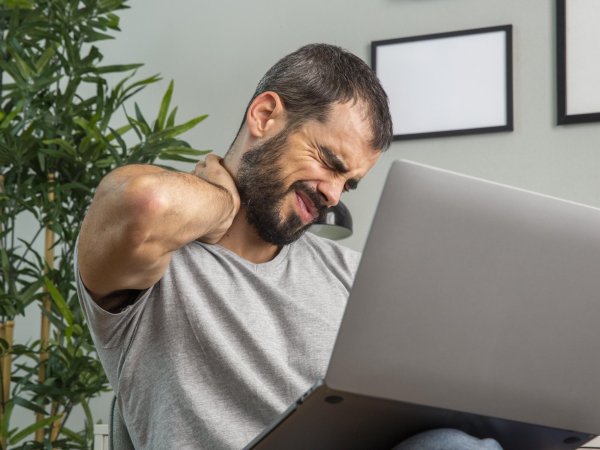 Hombre con dolor en el cuello, sentado ante un ordenador portátil.